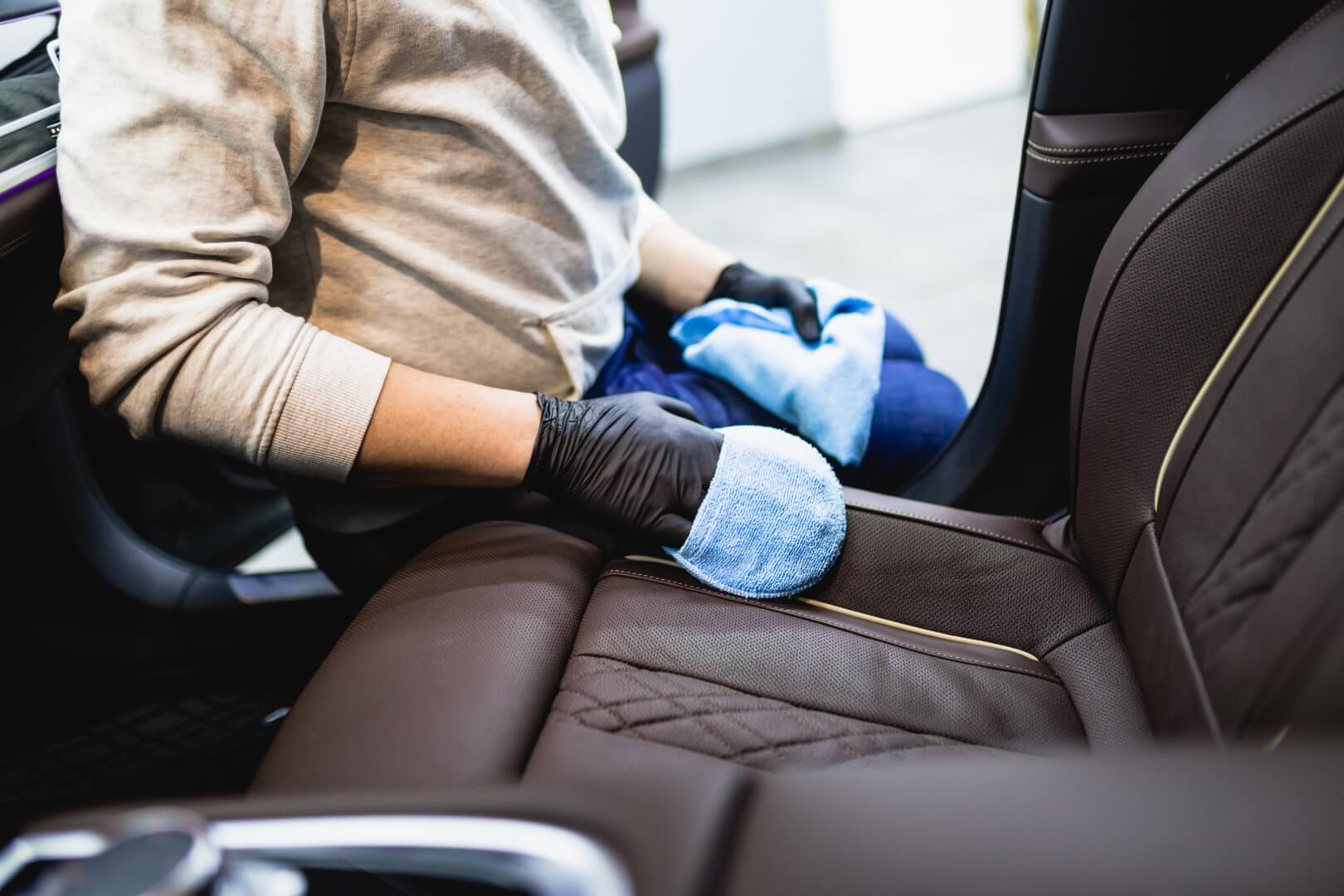 Image depicts a car detailing pro cleaning a car's seats.